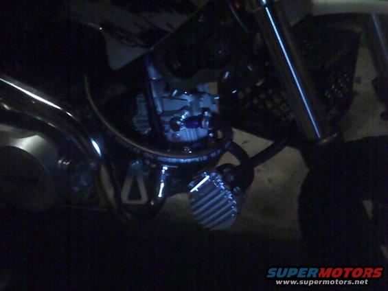 Close-up of a motorcycle's engine and exhaust system, showing hoses and some metal components