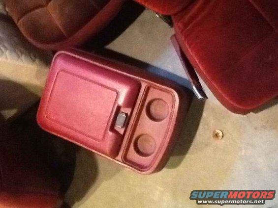 Red plastic center console with a flip-top compartment and two cup holders, next to a red seat