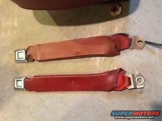 Two red seat belts with metal buckles and mounting points on a textured surface