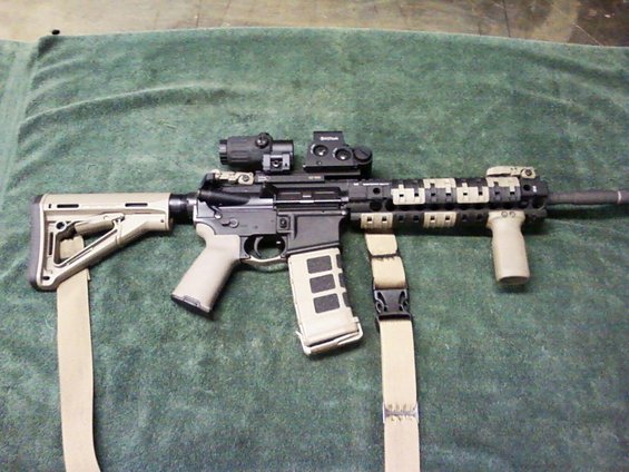 Assault rifle with tan stock and grip, black receiver, and tan camouflage handguard, resting on a green cloth
