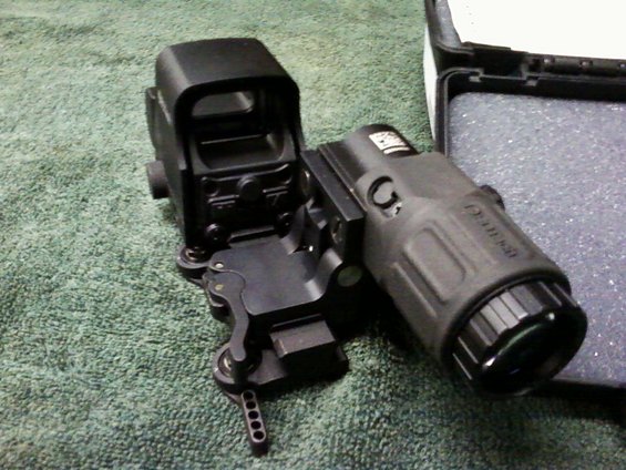 Black gun sight with a rectangular lens and a cylindrical lens, mounted on a textured surface