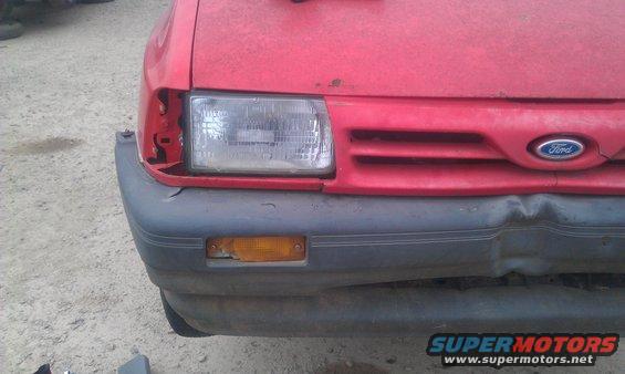 Red car front end with damaged headlight and bumper. Ford logo visible on grille
