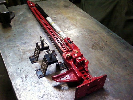 Red hi-lift jack with two black mounting brackets on a metal workbench