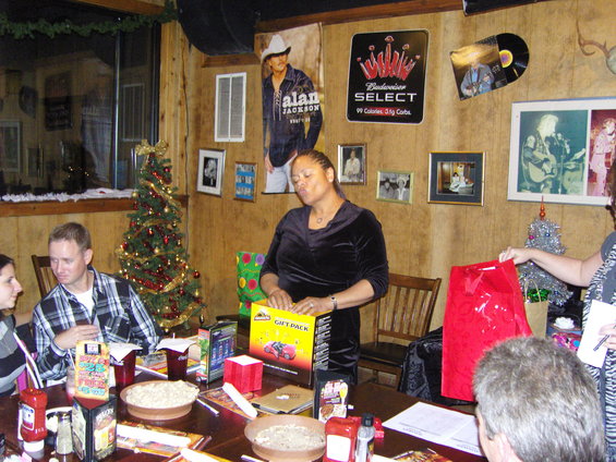 People gathered around a table with food and gifts, a Christmas tree is visible