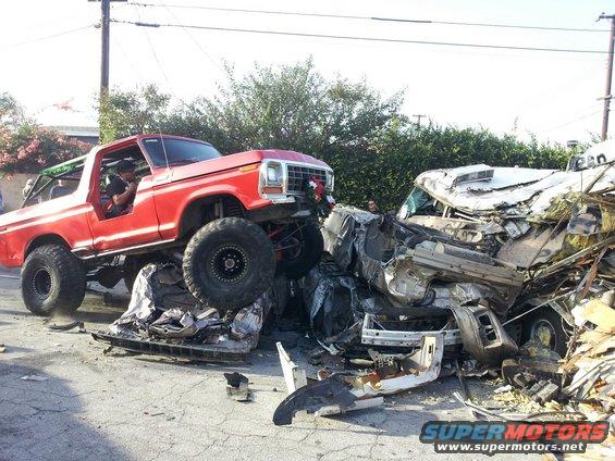 Red 1978 Ford Bronco with large tires on top of a severely damaged white car