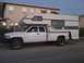 1997 Dodge 3500 - A white pickup truck is fitted with a large camper shell, extending over the bed and cab.