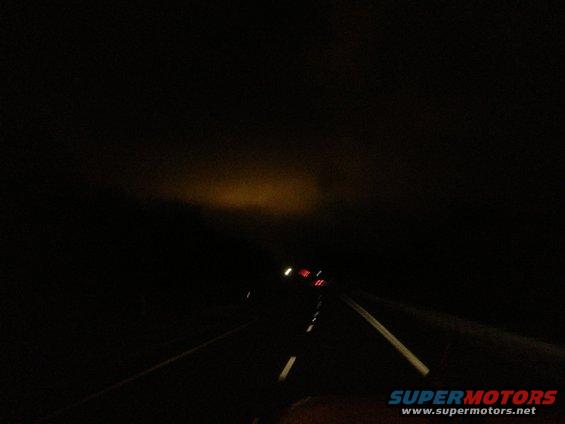 Dark road at night with headlights visible in the distance and a watermark
