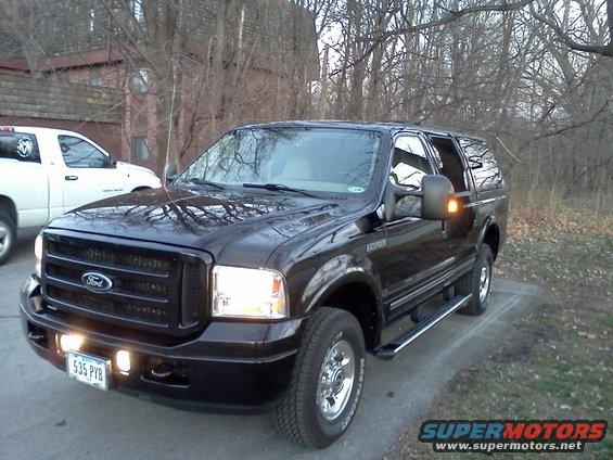 Black 2005 Ford Excursion parked on a driveway, front 3/4 view. A white pickup truck is visible to the left