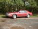 1992 Lincoln Mark VII - This red 1992 Lincoln Mark VII coupe is seen from a 3/4 front angle on a gravel surface with trees behind it.