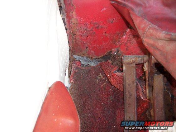 Red car interior floor with significant rust and damage, showing worn red carpet and metal supports