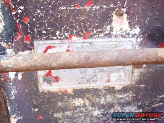 Close-up of a rusty metal plate with faded text, attached to a peeling painted surface