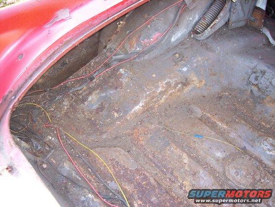 Red car trunk interior with extensive rust and exposed wiring