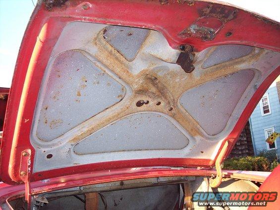 Underside of a red car hood showing rust and structural bracing
