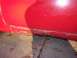 1956 Ford Thunderbird - The lower portion of a red car door exhibits significant rust and damage.