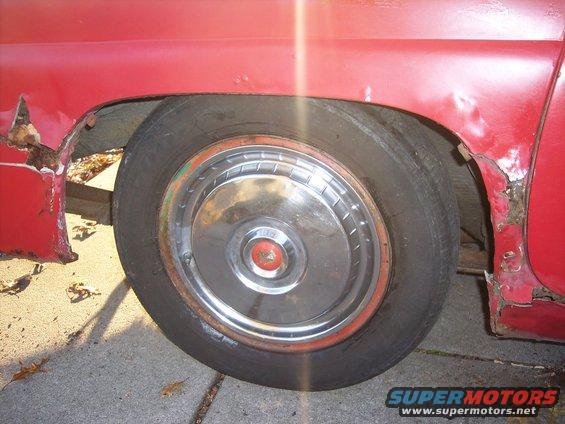 Red car's rear wheel well showing a rusty fender and hubcap