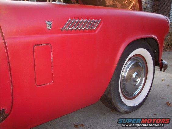 Red car fender with a chrome emblem and vent, showing a flat tire with a whitewall