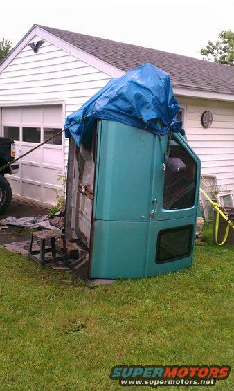 Teal truck cab lying on its side in a yard, covered partially by a blue tarp