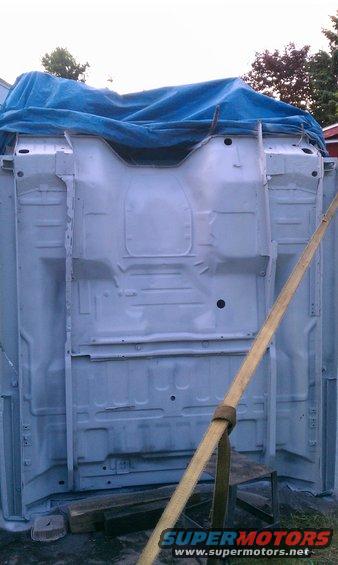 Vehicle frame upside down, covered by a blue tarp. A yellow strap is attached