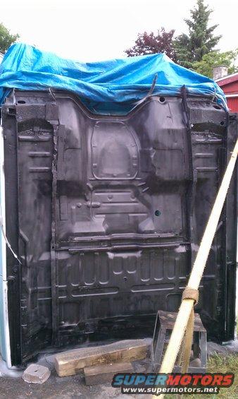 Black truck frame upside down, covered partially by a blue tarp. Wood blocks support it