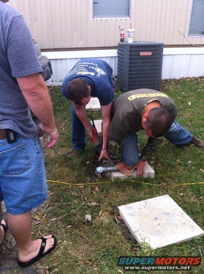 Three men working on a metal pipe on the ground outside a building
