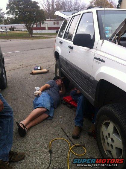 Two guys working under a white Jeep Grand Cherokee, one lying on the ground