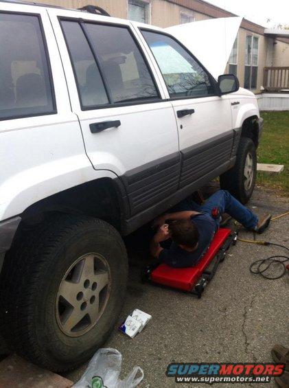 White Jeep Grand Cherokee with hood open, person on creeper working underneath