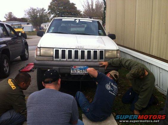 White Jeep Grand Cherokee with a Texas license plate, front view, with several people working on it