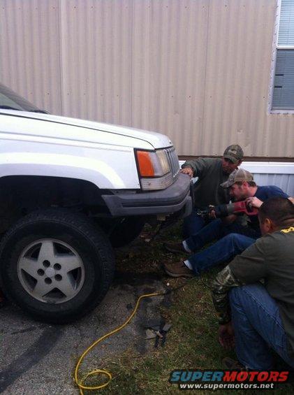 White Jeep Grand Cherokee front quarter panel and wheel, men working on bumper