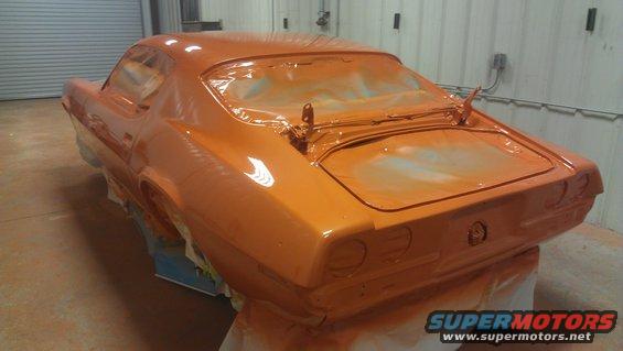 Rear view of an orange muscle car, possibly a 1970s model, being prepped for paint. The windows are covered with plastic
