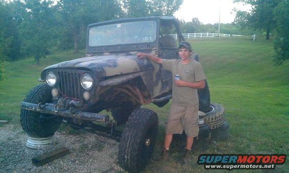 Modified Jeep CJ with large tires, camouflage paint, and a person standing next to it