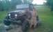 1987 Ford Bronco - Person stands next to a heavily modified Jeep CJ with oversized tires and camouflage paint.