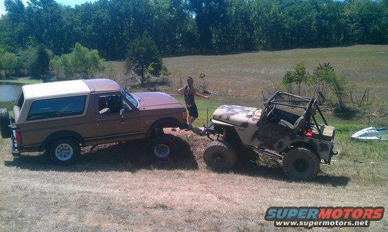 Brown Ford Bronco being towed by a lifted Jeep off-road. Person standing between them