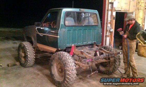 Green Ford Bronco with large tires and exposed frame, undergoing modification