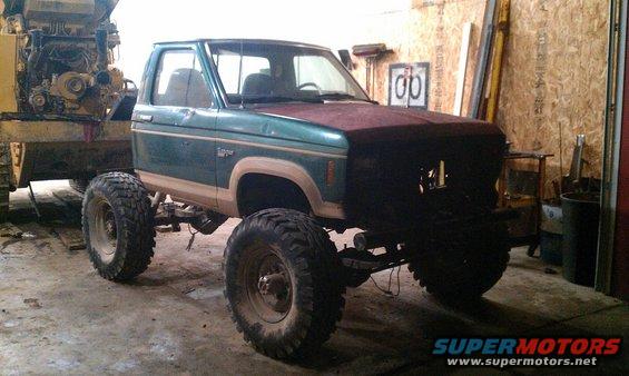 Lifted pickup truck with large tires in a garage, next to heavy equipment