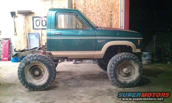Green Ford Ranger pickup truck with large tires and lifted suspension, missing its bed