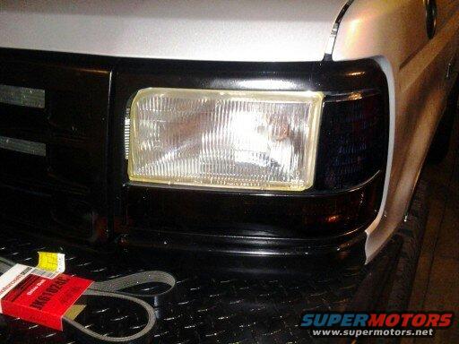 Close-up of a 1992 Ford F-Series truck's front grille and headlight assembly. A new serpentine belt is in its red box on the diamond plate bumper