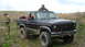 1986 Ford Bronco - A black Ford Bronco sits in a grassy field with two men nearby, one on the roof and another looking at a device.