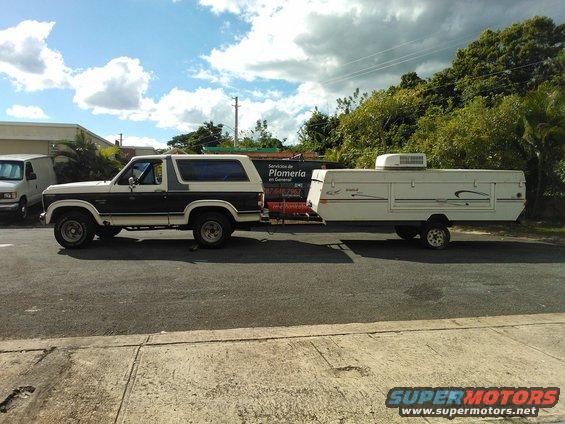 Two-tone Ford Bronco with a pop-up camper trailer attached, side view