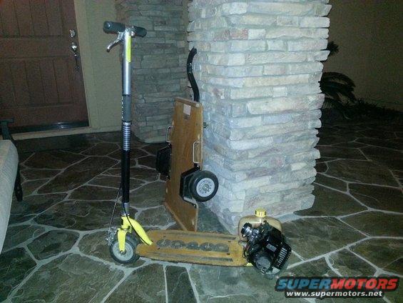 Yellow motorized scooter with a gas engine attached to the deck, leaning against a stone pillar