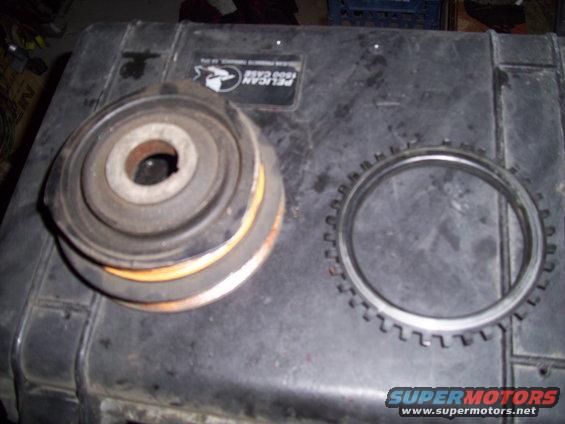 Two automotive parts, a rubber and metal bushing and a toothed metal ring, rest on a black case