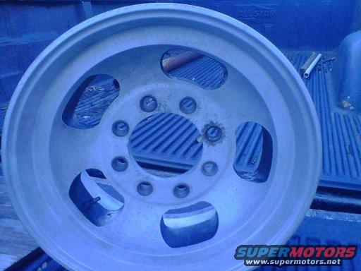 Silver wheel with five large cutouts and ten lug nut holes, resting in a blue truck bed