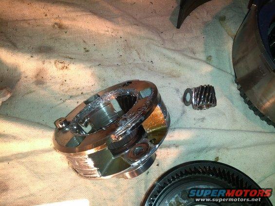 Damaged metal transmission components, including a gear and a ring, are spread out on a cloth surface. Metal shavings are visible
