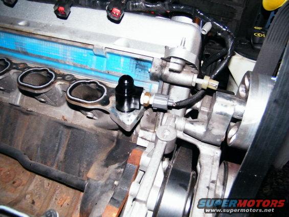 Black sensor attached to a metal engine component with visible exhaust manifold ports