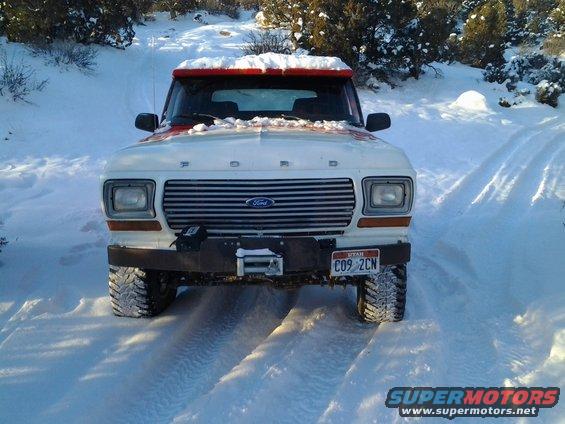 White Ford Bronco with red trim in snow, front view. Aftermarket bumper with winch
