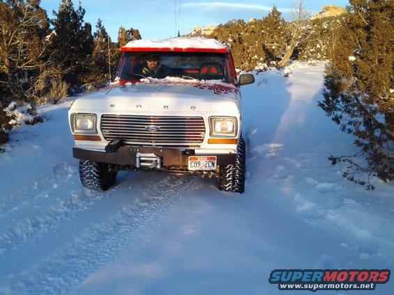 1979 Ford Bronco driving on a snowy road with trees on either side