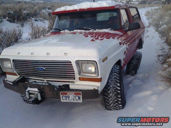 White and red Ford Bronco with flame decals driving on a snowy road. It has a winch on the front bumper