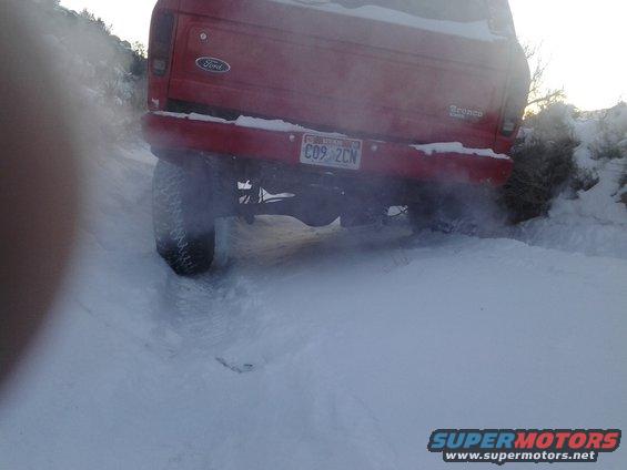 Red 1979 Ford Bronco rear view driving in snow
