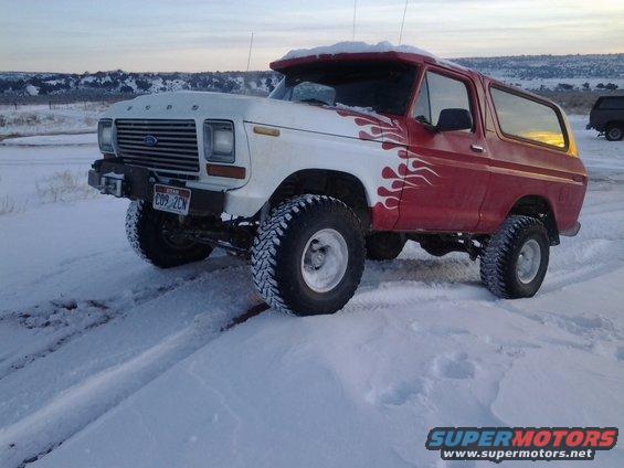 White and red Ford Bronco with flame decals parked in snow, another vehicle visible in background