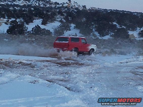 Red and white 1979 Ford Bronco driving through snow and mud