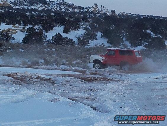 Red and white SUV with flame decals driving through snow and mud. Appears to be a 1978 Ford Bronco